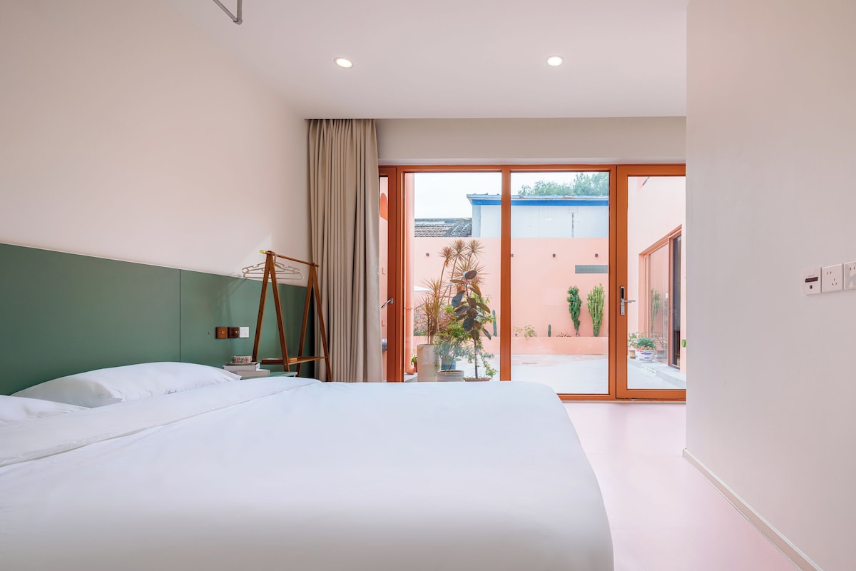 Habitación de hotel con una cama grande, un perchero de madera, una ventana con cortinas y vistas al exterior.