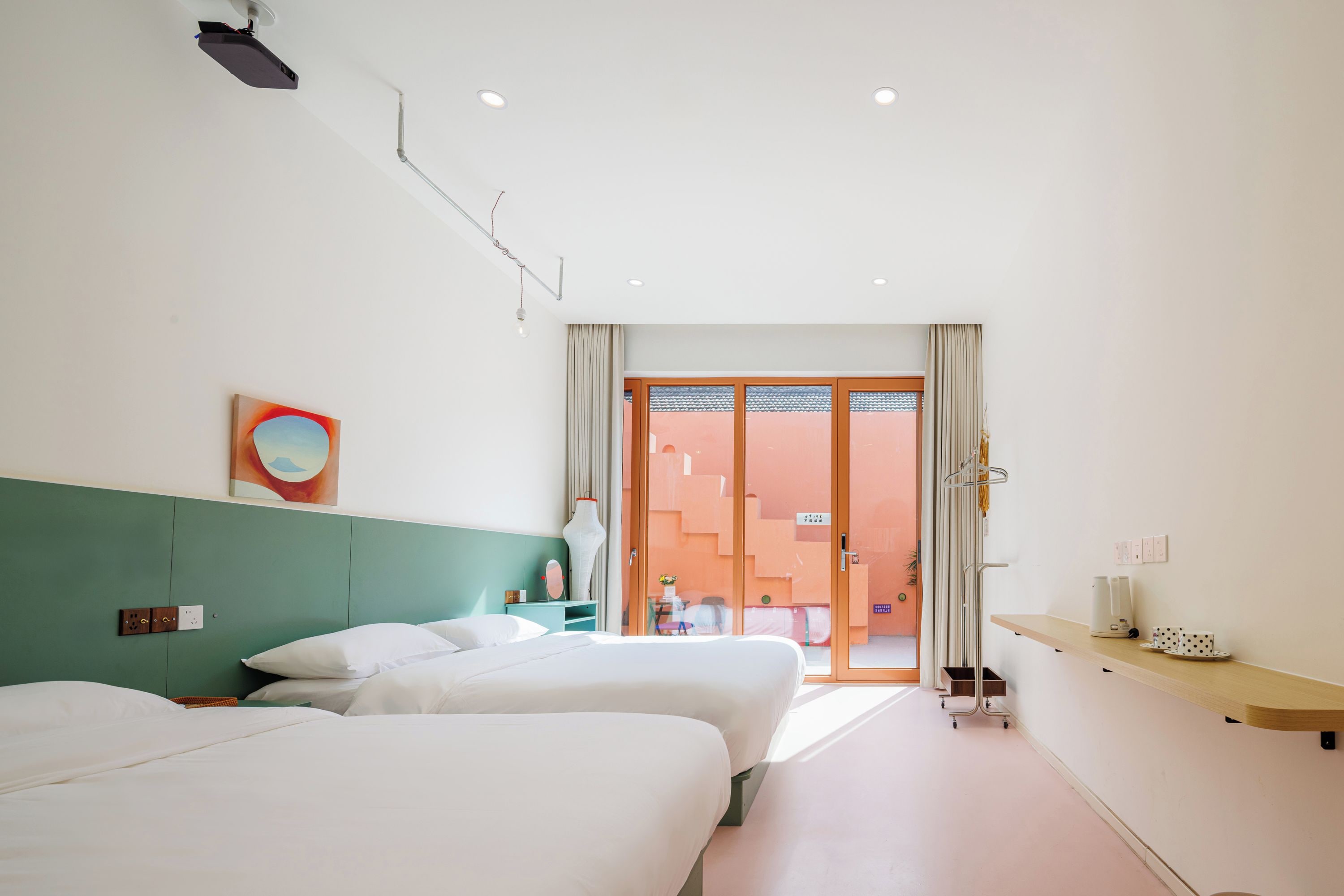 A hotel room with two beds, a small table, a vase, and a view of the outside.