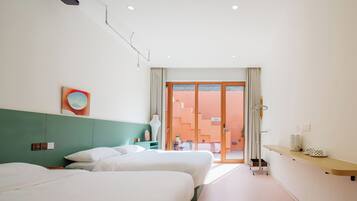 A hotel room with two beds, a small table, a vase, and a view of the outside.