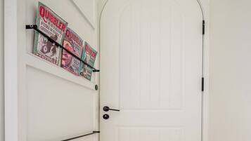 A white door with a black handle, a white wall with a shelf holding several Quibbler magazines, and a black cable running along the wall.