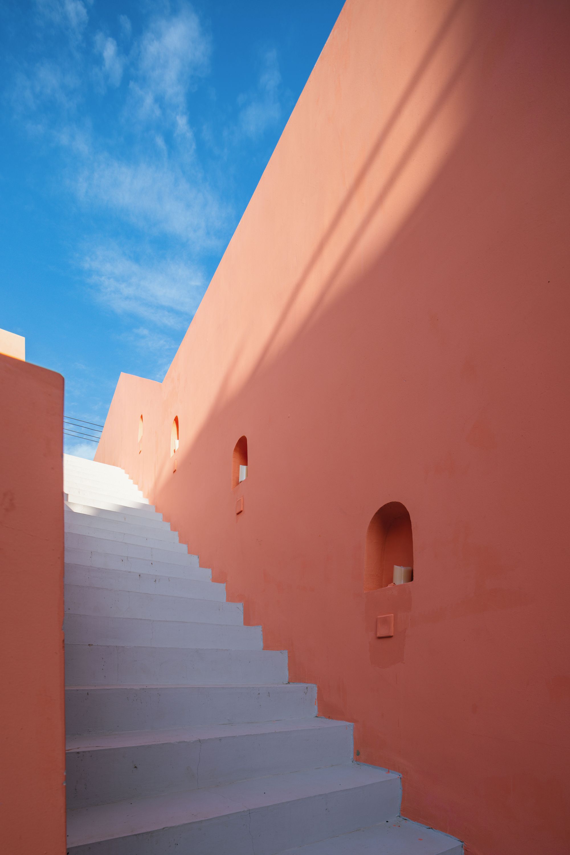 A staircase leading up to a building with pink walls and small windows.