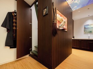 Habitació amb terra de fusta, una estant per abrics amb un abric fosc, una escombra i un quadre encimbellat a la paret.