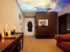 A room with a wooden floor, a desk with a book and candles, a robe hanging on the wall, and a ceiling mural. - Rons Wizardry Healing Homestay (Tongzhou)