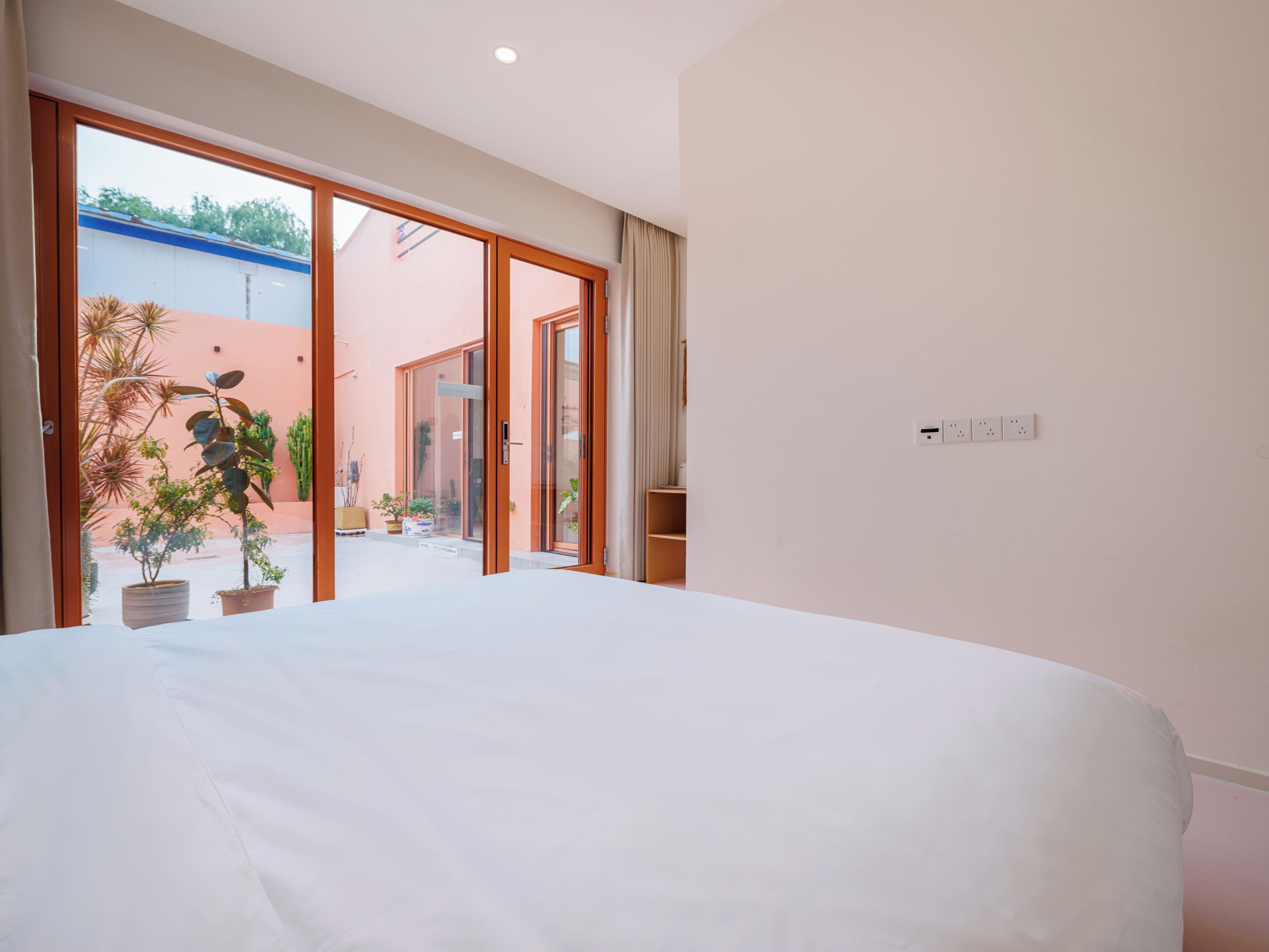 A hotel room with a large bed, sliding glass doors leading to a balcony with potted plants.