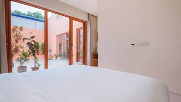 A hotel room with a large bed, sliding glass doors leading to a balcony with potted plants.