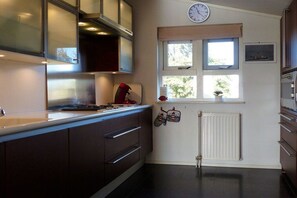 A kitchen with dark cabinets, a clock, a window with blinds, and a radiator. - Friesland Zilverreiger 4 (JK Workum)
