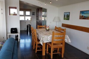 Ein Essbereich mit einem Tisch für vier Personen, Holzsesseln, einem blauen Sofa und einer Wandleuchte.