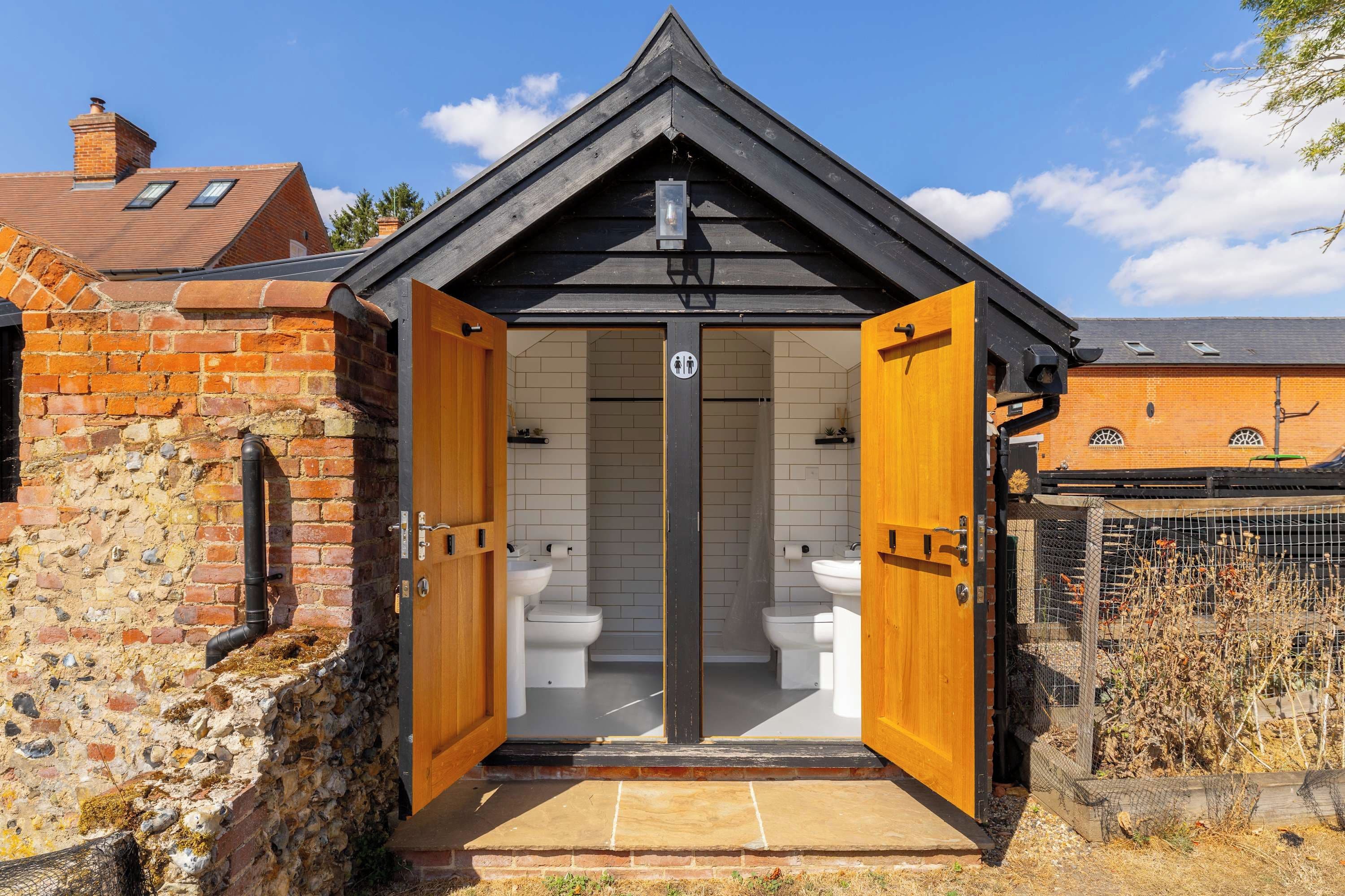 A small, private bathroom with two toilets, a shower, and a sink.