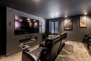 Un cinema privat amb un televisor pla gran, butaques de pell reclinables, una llar de foc i pòsters de pel·lícules emmarcats a la paret.