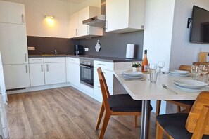 A modern kitchen with white cabinets, a stove, and a dining area with a table set for two. - Holiday apartment with 1 bedroom (Kressbronn)