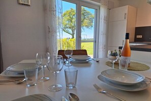A dining table set with plates, glasses, and cutlery, with a view of trees and grass through the window. - Holiday apartment with 1 bedroom (Kressbronn)