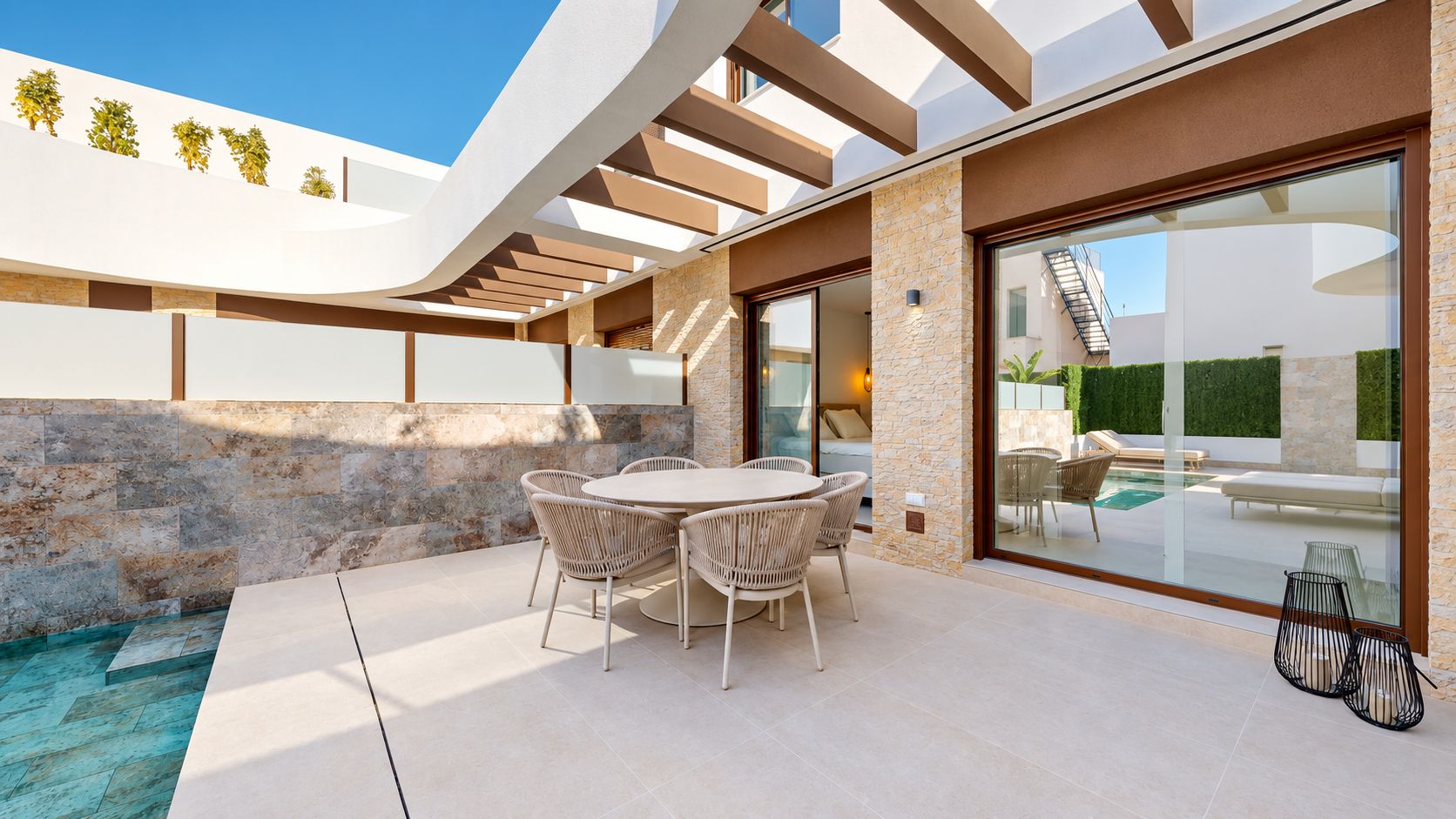 Um pátio moderno ao ar livre com uma mesa redonda e cadeiras, uma piscina e um vão de vidro que dá para a área da piscina.