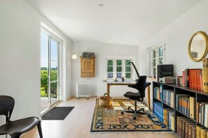 A room with a large window, a desk, a chair, a bookshelf, and a radiator. - Thatched timber-framed house by meadow and stream (Balle)