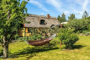 A traditional house with a thatched roof, a hammock in the yard, and a well-maintained garden. - Thatched timber-framed house by meadow and stream (Balle)