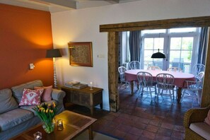 A cozy living room with a sofa, coffee table, and a dining area with a table and chairs. - Holiday home de Broodkiste (Domburg)