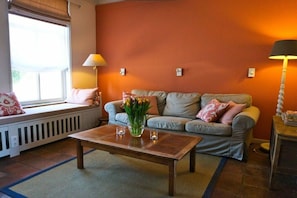 A living room with a sofa, a coffee table, and a window with blinds. - Holiday home de Broodkiste (Domburg)