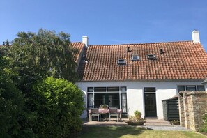 A house with a tiled roof, a front door, and a small garden with a table and chairs. - Holiday home de Broodkiste (Domburg)