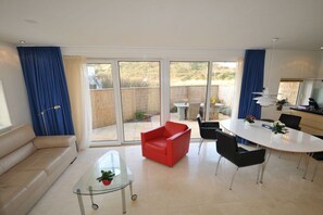 Ein modernes Wohnzimmer mit einem Glastisch, einem roten Sessel und einem Essbereich mit weißem Tisch und Stühlen.