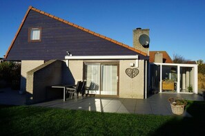 Una casa moderna con techo inclinado, una antena parabólica y un patio con mobiliario exterior.