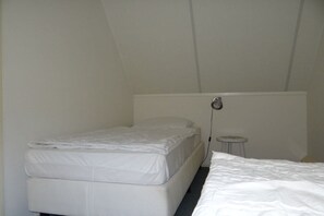 A small, single-bed room with a white mattress and a single bedside table. - Holiday home with 3 bedrooms (Oostkapelle)