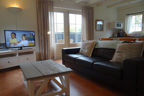 A living room with a television, a sofa, a coffee table, and a kitchen area in the background. - Holiday home with 3 bedrooms (Oostkapelle)