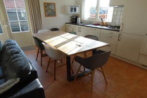 A compact living space with a dining table, chairs, a sofa, a kitchen area with cabinets and appliances, and a window providing natural light. - Holiday home with 3 bedrooms (Oostkapelle)