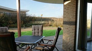 Un patio al aire libre con una mesa y sillas, un muro de ladrillo y vistas a una zona verde.