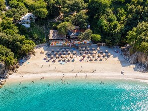 An aerial view of a beach with a building featuring a colorful mural, surrounded by umbrellas and beachgoers. - Secret Garden Volos - Tranquil Private Retreat (Volos)
