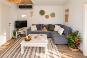 A modern living room with a grey sofa, a flat-screen TV, and decorative wall art. - Secret Garden Volos - Tranquil Private Retreat (Volos)