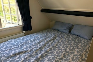 A small, single-bed room with a sloped ceiling, a window with curtains, and a radiator. - Holiday home de Koektrommel (Domburg)