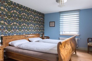 Ein Zimmer mit einem Bett, einem Heizkörper, einem Fenster mit Jalousien und einer Wand mit Muster.