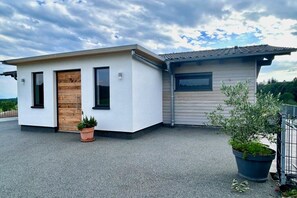 A modern two-story building with a flat roof, a wooden door, and a small attached structure with a window. - Schottenhof Walser 3 (Achberg)