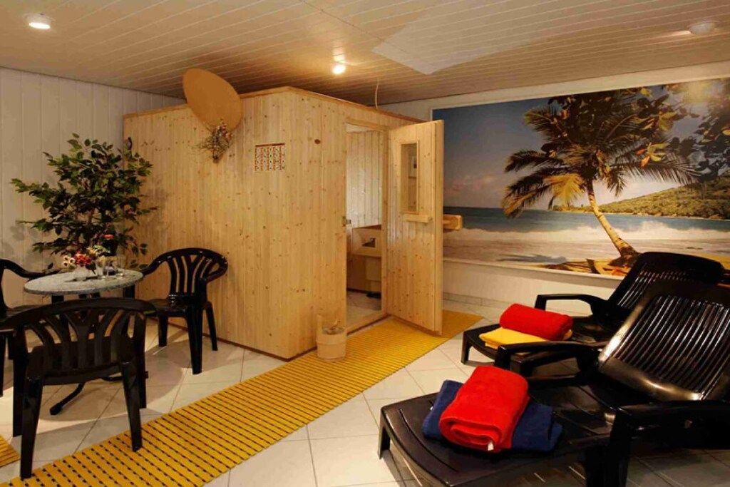 A room with a wooden partition, a dining area with chairs, a table, and a massage chair with towels.