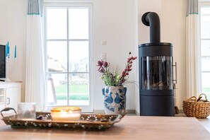 Ein Zimmer mit einem schwarzen Holzofen, einer Blumenvase, einer Kerze und einem Korbwäschekorb.