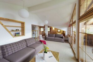 A modern living room with a sofa, a coffee table with a vase, and a dining area in the background. - Holiday apartment in Zell am See with Wi-Fi (Zell am See)