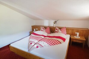 A single bed with a wooden headboard, a bedside table with a lamp, and a small nightstand with a vase of flowers. - Holiday apartment in Zell am See with Wi-Fi (Zell am See)