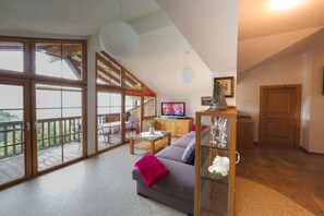 A spacious living area with a sofa, a coffee table, and a television. There is a balcony with a view of greenery. - Holiday apartment in Zell am See with Wi-Fi (Zell am See)