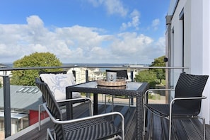 A balcony with a table and chairs, a view of the sea, and a building in the background. - Holiday apartment in Glowe with sauna (Glowe)