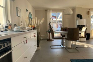 A modern kitchen with white cabinetry, a dining area with a table and chairs, and a large window with curtains. - Holiday home with 2 bedrooms (Kramerhof OT Parow)
