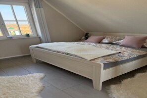 A bedroom with a sloped ceiling, a bed with a floral bedspread, and a window with a view of the outside. - Holiday home with 2 bedrooms (Kramerhof OT Parow)