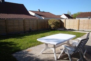 Eine Terrasse mit weißem Tisch und Stühlen, umgeben von einem Holzzaun und einem Rasen.
