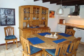 Ein Essbereich mit Holztisch und Stühlen, einem Holzschrank mit Glastüren sowie einer Küche im Hintergrund.