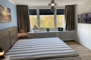 A bedroom with a bed, a window with curtains, a radiator, and a wall-mounted lamp. - Baltic Sea Dream 139 (Travemünde)