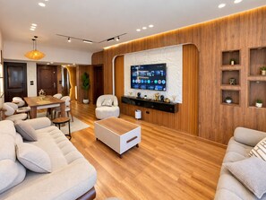 A modern living room with a flat-screen TV mounted on the wall, a dining area with a wooden table, and a seating area with sofas and a coffee table. - 3BRs Mohandessin Modern Living (Giza Governorate)