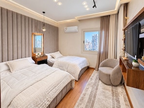 A hotel room with two beds, a TV, a chair, a window with a city view, and an air conditioning unit. - 3BRs Mohandessin Modern Living (Giza Governorate)