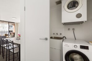 A compact laundry room with a front-loading washing machine, a sink, and a small window. - Spacious 2-Bed Apartment Near Parramatta CBD (Parramatta)