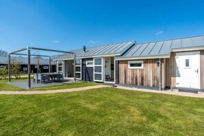 Ein modernes Gebäude mit einer überdachten Terrasse, großen Fenstern und einem Metalldach.