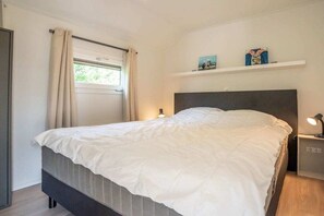 Ein Schlafzimmer mit einem Bett, einem Nachttisch, einem Regal mit Gegenständen, einem Fenster mit Vorhängen und einer Tür.