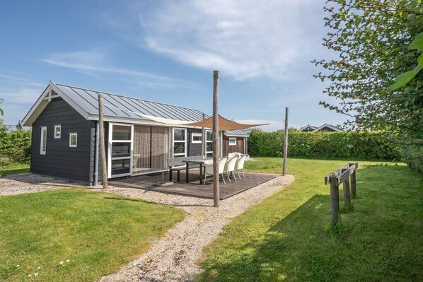 Ein modernes Haus mit überdachter Terrasse, Kiesweg und Holzzaun.