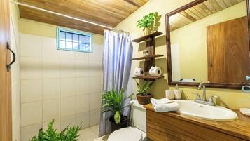 Un baño con techo de madera, inodoro, lavamanos, espejo y ventana con cortina.